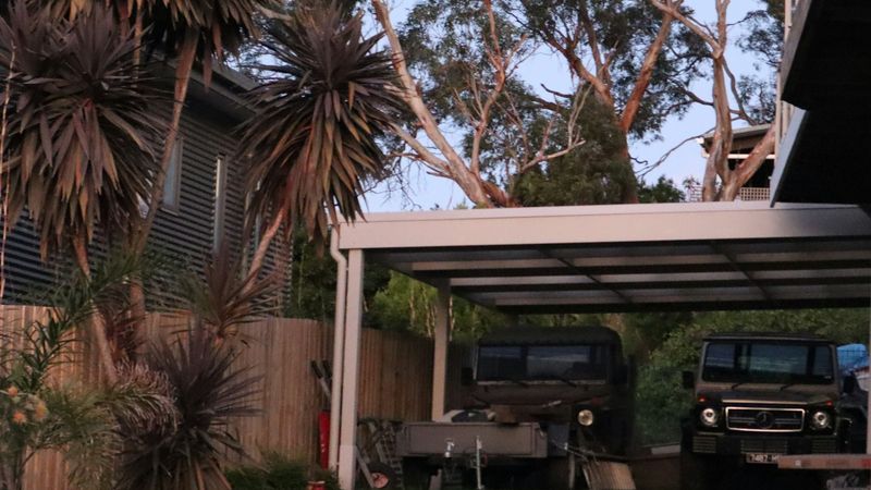 Abri véhicule à toiture claire, dans un jardin, avec deux 4×4 stationnés dessous
