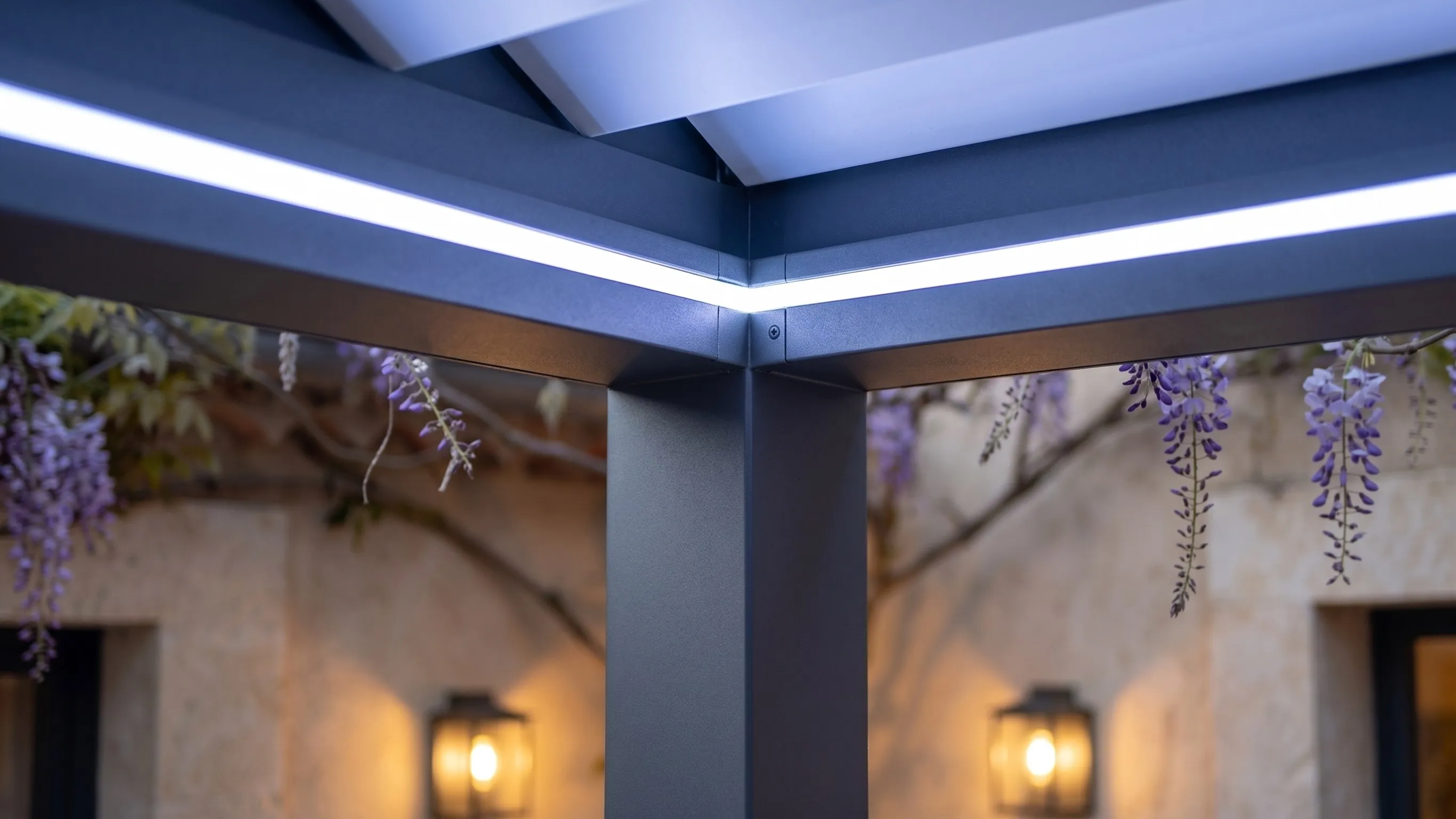 Pergola bioclimatique adossée à un mas en pierre, bandeau LED intégré à la traverse et glycine en fleur — vue d’illustration